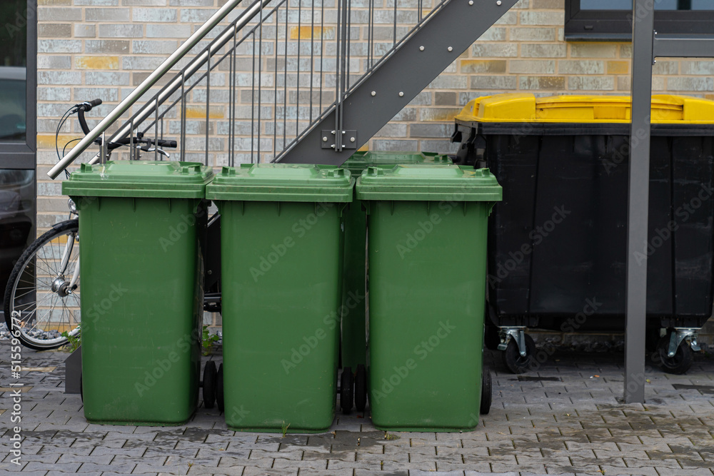 Three green trash cans in front of a residential building. Three green trash cans in front of a residential building.