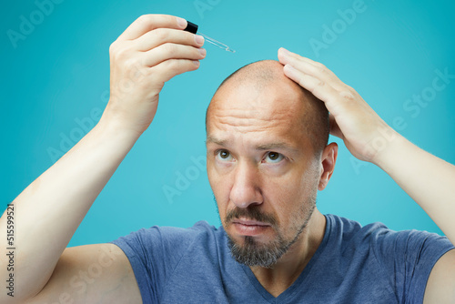 Close up image of  bearded man with pipette with beard oil on blue background.