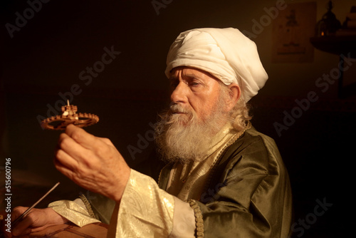 Old Islamic Scientist is Examining a Wooden Gear photo