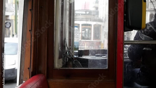 Driver cabin in a Lisbon tram commute. Ride around the European city streets. Vintage wooden cabin interior and red leather seats. Driver spins speed control handle. Other controls on dashboard.