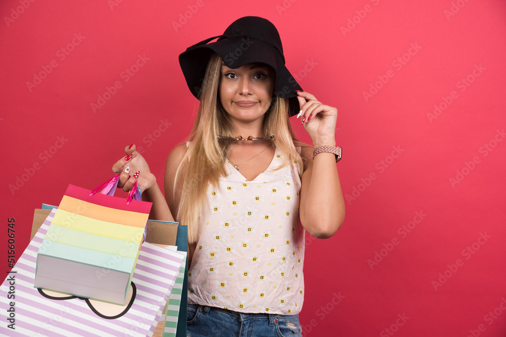 Confused woman with hat holding her shopping bags on red background Confused woman with hat holding her shopping bags on red background