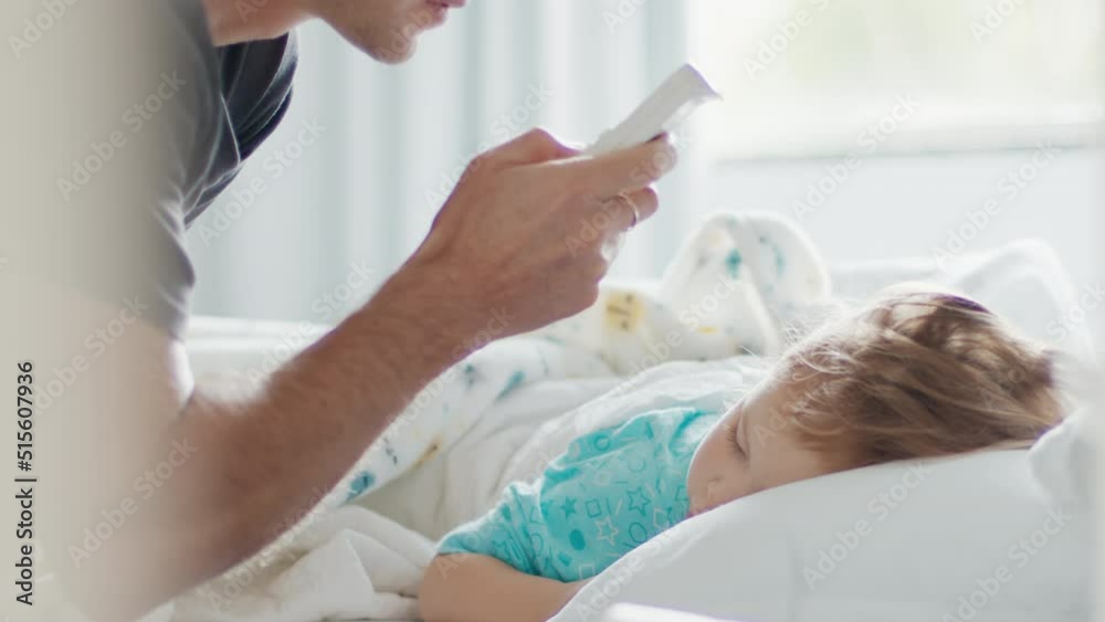 Child care. Father adjusts room's temperature with AC remote control and removes warm blanket from the sleeping kid Child care. Father adjusts room's temperature with AC remote control and removes warm blanket from the sleeping kid
