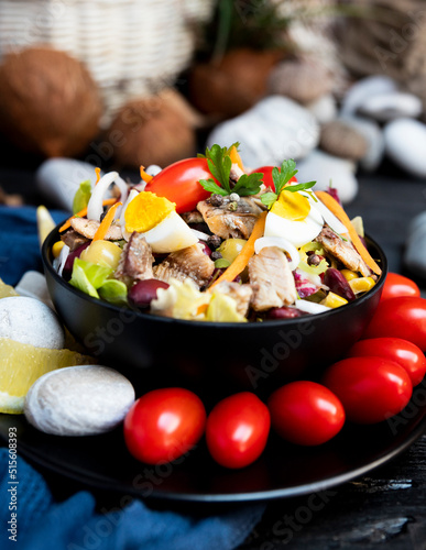 Fish salad with sardines, harringe, tuna, tomato, lemon, lettuce, cabbage, olives, beans, corn, carrotes and eggs on rustic kitchen table photo