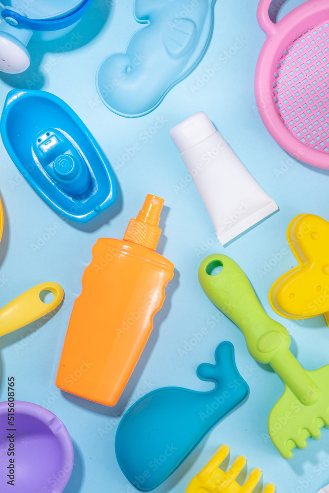Fototapeta premium Baby Sunscreen suncare concept. Suntan lotion bottles with kids vacation accessory, sand molds, panama hat, on light blue background copy space