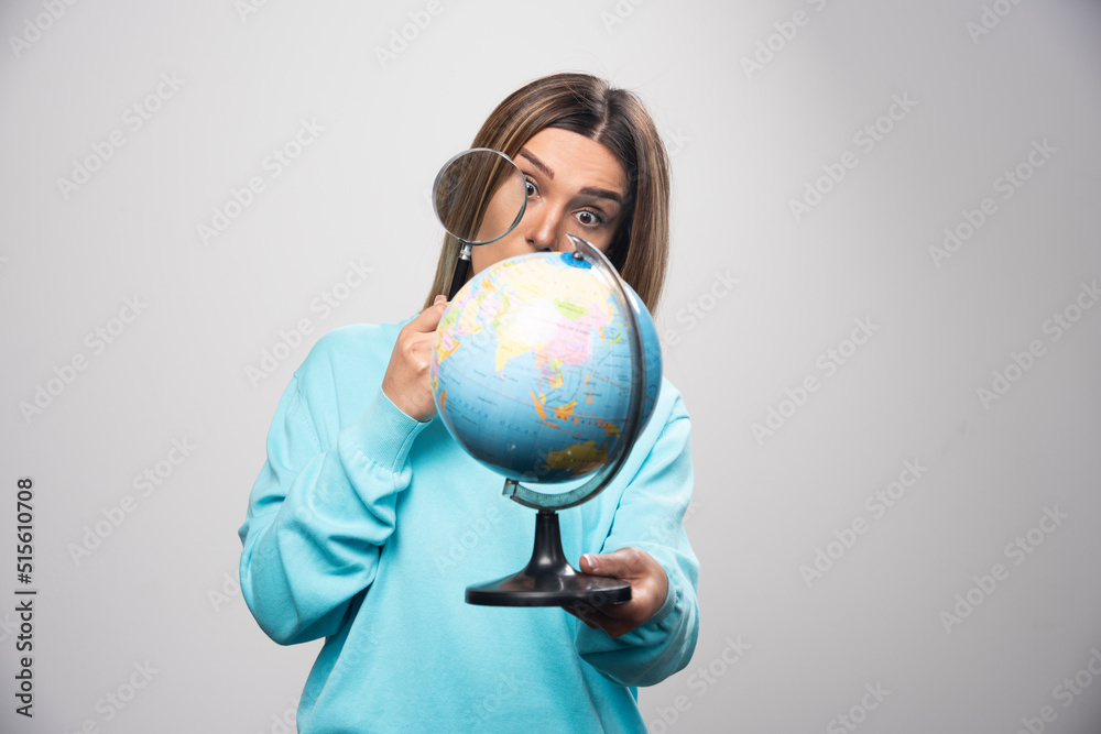 Blonde girl in blue sweatshirt holding a globe and looking for a destination with magnifier Blonde girl in blue sweatshirt holding a globe and looking for a destination with magnifier