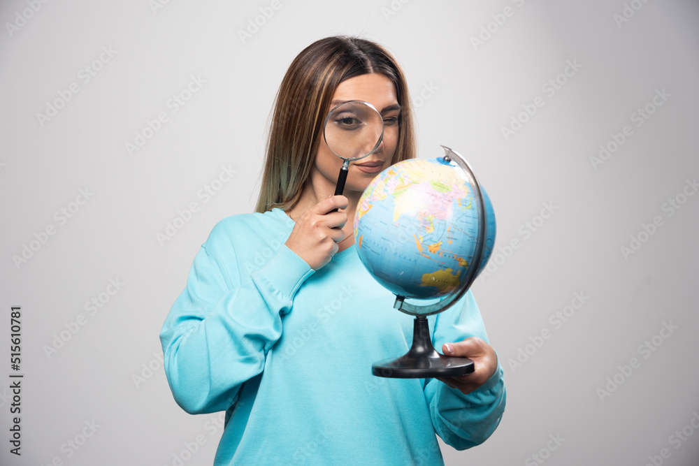 Blonde girl in blue sweatshirt holding a globe and looking for a destination with magnifier Blonde girl in blue sweatshirt holding a globe and looking for a destination with magnifier