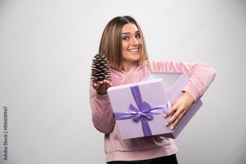 Blonde lady in pink sweatshirt takes out an oak tree cone from the gift box and feels happy Blonde lady in pink sweatshirt takes out an oak tree cone from the gift box and feels happy