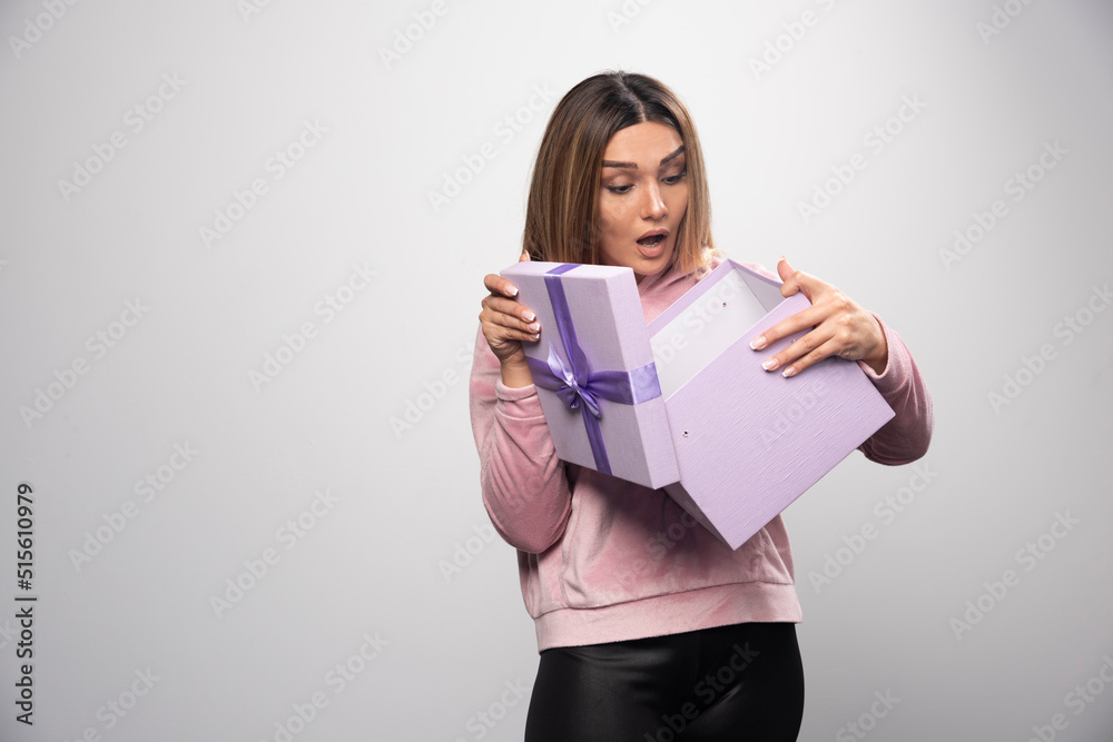 Blonde lady in pink sweatshirt opens up a gift box and gets surprized Blonde lady in pink sweatshirt opens up a gift box and gets surprized