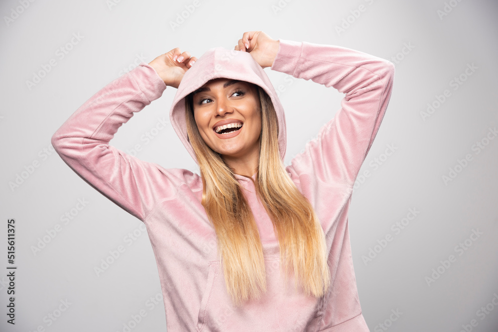 Blonde lady in pink sweatshirt making joyful and positive poses by wearing hoodie to her head Blonde lady in pink sweatshirt making joyful and positive poses by wearing hoodie to her head