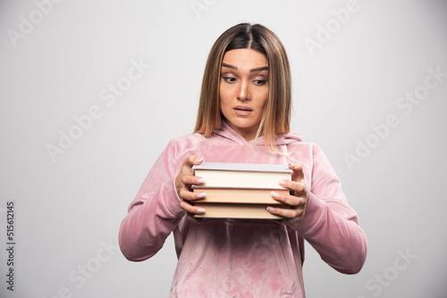 Girl in pink swaetshirt holding and carrying heavy pile of books