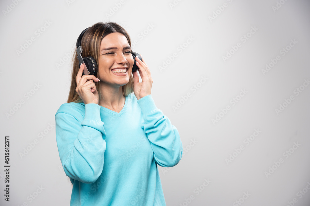 Blonde girl in blue sweatshirt wearing headphones, enjoying the music and having fun Blonde girl in blue sweatshirt wearing headphones, enjoying the music and having fun