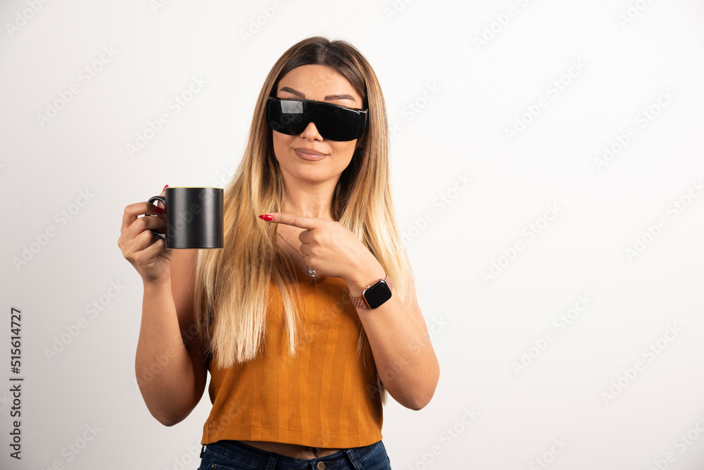 Young woman pointing at black cup and wearing goggles Young woman pointing at black cup and wearing goggles