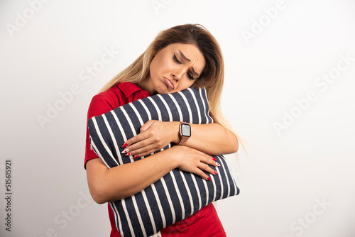 Upset young woman in red shirt hugging pillow over white background