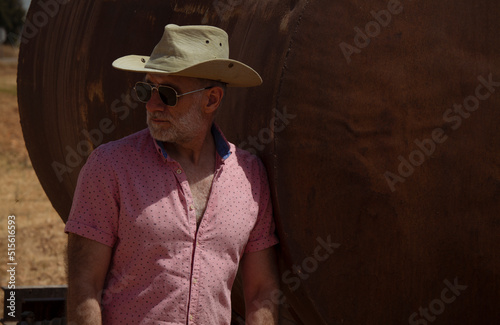 Portrait of adult man in cowboy hat and sunglasses against water tank in fields © WeeKwong
