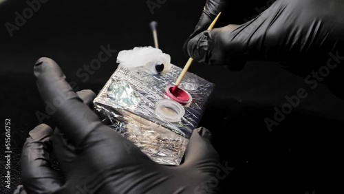 Hands in black latex gloves stir the paint for permanent makeup. Close-up.