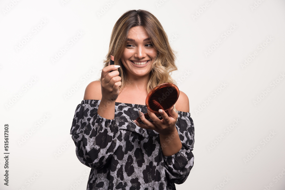 Young woman applying lipstick on white background with happy expression Young woman applying lipstick on white background with happy expression