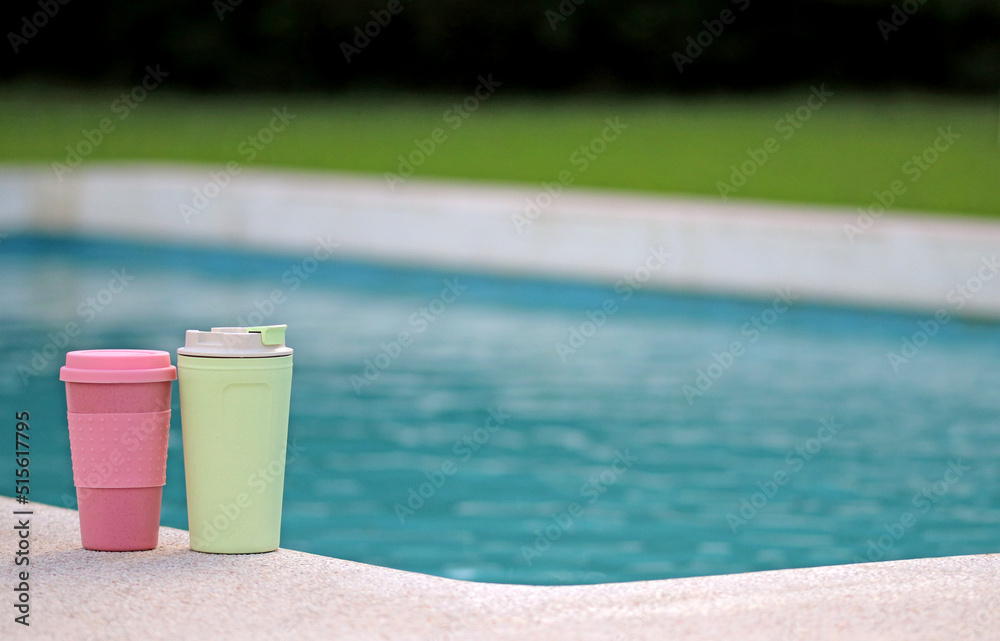 Two recyclable plastic cups next to a swimming pool Two recyclable plastic cups next to a swimming pool