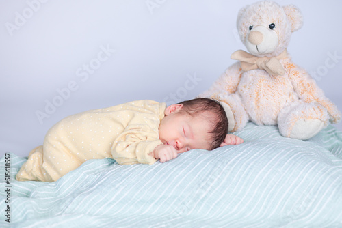 a newborn baby sleeps on a pillow next to a bear sits
