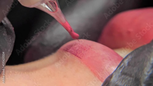 Close-up of a permanent makeup procedure. A needle pierces the lips and injects paint under the skin. Macro photo