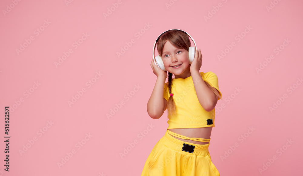 Funny child girl in yellow posing isolated on pink background. Mock up copy space. Listen music with headphones Funny child girl in yellow posing isolated on pink background. Mock up copy space. Listen music with headphones