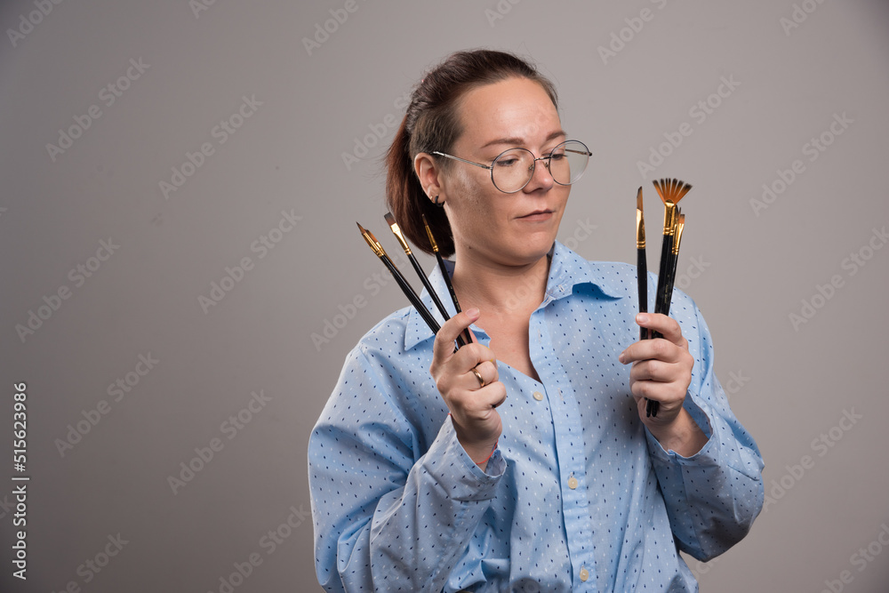Woman artist holds painting brushes on gray background Woman artist holds painting brushes on gray background