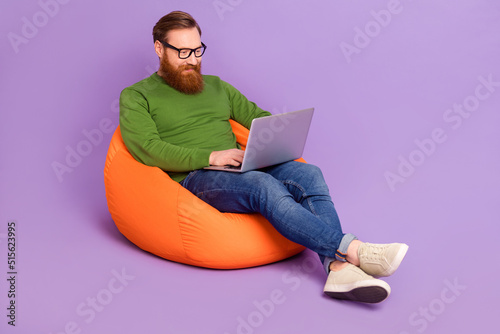 Full body photo of handsome intelligent guy sitting bag use wireless netbook isolated on violet color background