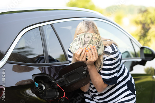 Desperate woman hides face behind cash near an open car fuel tank, concept of rising fuel prices photo