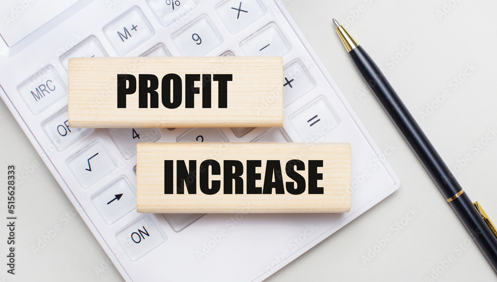 Wooden blocks with the PROFIT INCREASE Iie on a light background on a white calculator. Nearby is a black handle. Business concept Wooden blocks with the PROFIT INCREASE Iie on a light background on a white calculator. Nearby is a black handle. Business concept