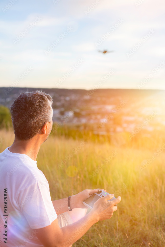 homme pilotant un drone avec une télécommande sur une colline au coucher du soleil