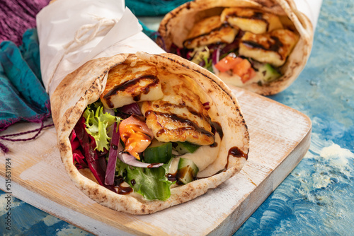 Traditional Mediterranean Arabic grilled halloumi, hummus and vegetables in flatbread wraps topped with herbs and balsamic vinegar
