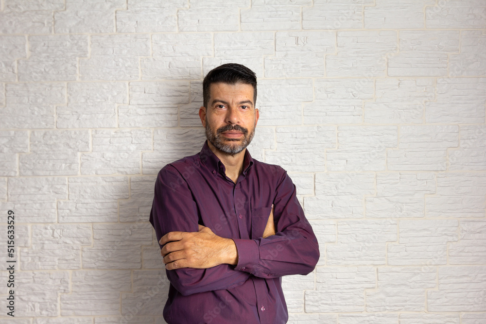 Portrait of middle aged man arms crossed and looking at camera with serious face. Isolated on white brick wall Portrait of middle aged man arms crossed and looking at camera with serious face. Isolated on white brick wall