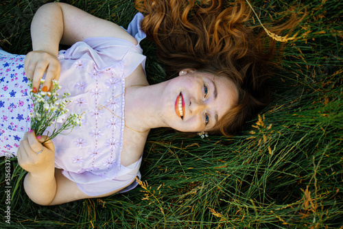 redhead portrait of a beautiful young sexy red-haired woman, lying in the spring sun, relaxing on the green grass.