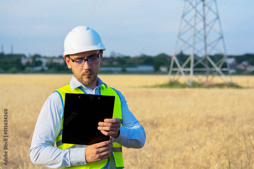 engineer in a helmet, glasses and a yellow vest, hand on a helmet, holding a notebook, a folder, making notes in a notebook a caucasian white engineer engineer in a helmet, glasses and a yellow vest, hand on a helmet, holding a notebook, a folder, making notes in a notebook a caucasian white engineer