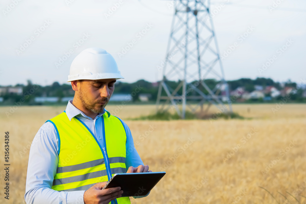 Fototapeta premium a male engineer in a helmet and goggles uses a smartphone for field work near a telecommunications tower that controls cellular electrical installations.