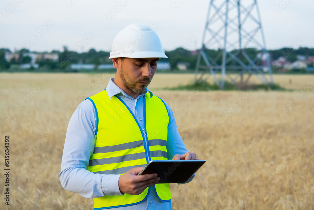 Fototapeta premium a male engineer in a helmet and goggles uses a smartphone for field work near a telecommunications tower that controls cellular electrical installations.