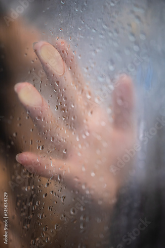 Fototapeta Naklejka Na Ścianę i Meble -  Female hand and unrecognizable silhouette behind wet glass in shower