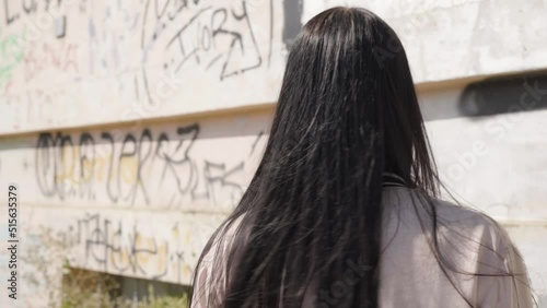 A young beautiful Caucasian woman turns around and looks at the camera - closeup - a wall with graffiti in the background