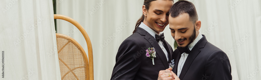 happy gay couple in suits with boutonnieres holding hands on wedding day, banner. happy gay couple in suits with boutonnieres holding hands on wedding day, banner.