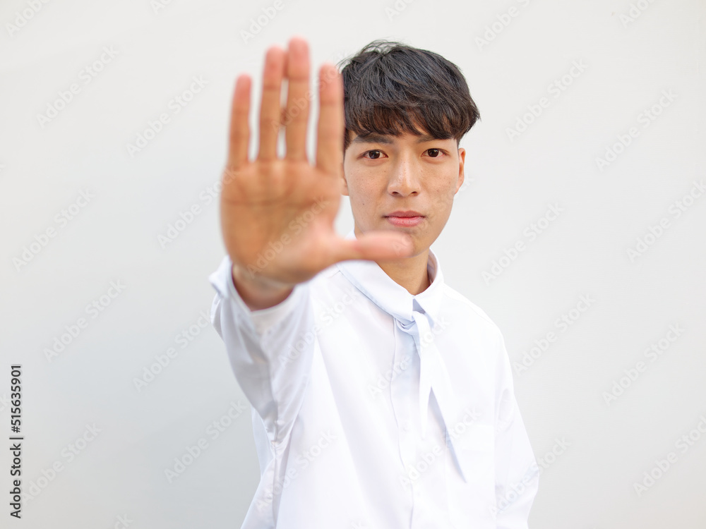Portrait of Chinese young man with black hair in white shirt posing against white background, hand out means no or stop gesture, front view focused on face, blurry hand. Portrait of Chinese young man with black hair in white shirt posing against white background, hand out means no or stop gesture, front view focused on face, blurry hand.