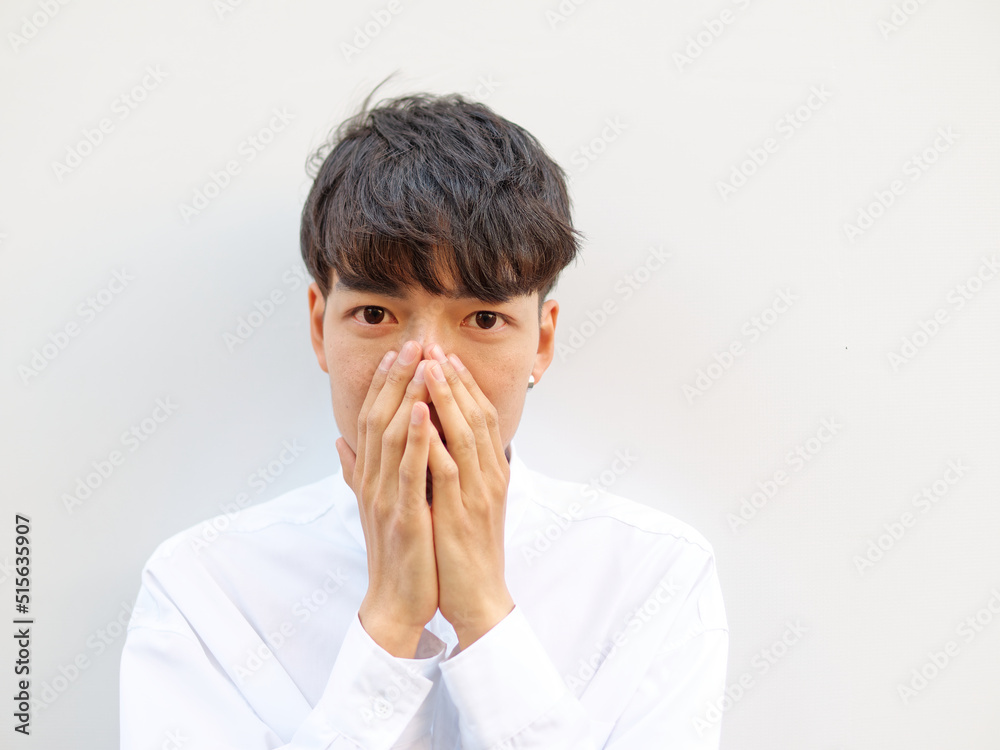 Portrait of Chinese young man with black hair in white shirt posing against white background, two hands cover his mouth and looking at camera with surprised or astonished expression, front view Portrait of Chinese young man with black hair in white shirt posing against white background, two hands cover his mouth and looking at camera with surprised or astonished expression, front view