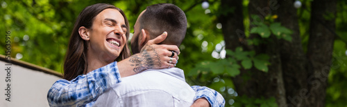Fotografiet tattooed gay man smiling and hugging boyfriend in summer, banner.