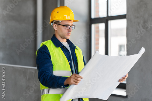 architecture, construction business and people concept - male architect in helmet with blueprint at office