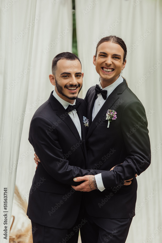 happy gay couple in suits with boutonnieres hugging during wedding ceremony.