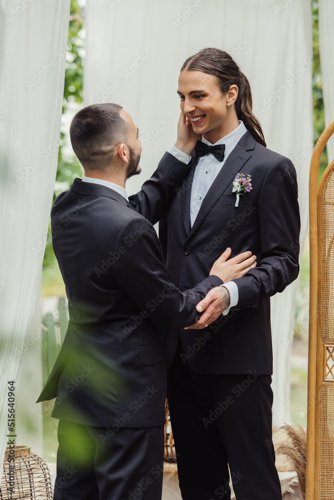 bearded gay man touching cheek of pleased groom on wedding day. bearded gay man touching cheek of pleased groom on wedding day.