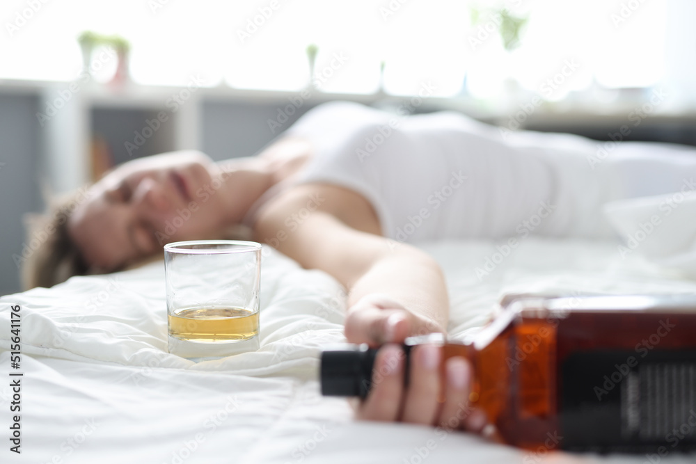 Drunk young woman lies in bed in bottle of alcohol Drunk young woman lies in bed in bottle of alcohol
