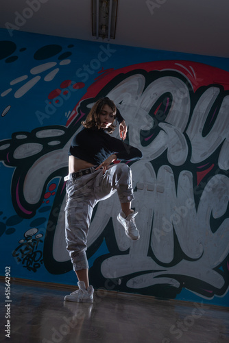 Silhouette of young woman hiphop dancer (breakdancer)dancing on graffiti studio background. Contrast colors.