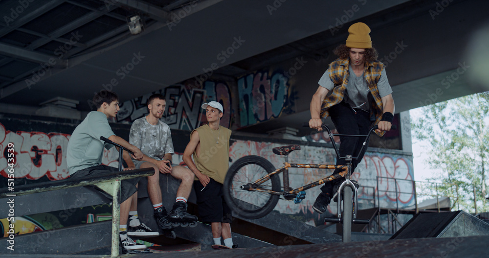 Active teens watching training on bmx bike at skate park with graffiti. Active teens watching training on bmx bike at skate park with graffiti.