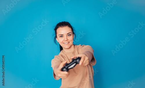 A cheerful girl in a beige T-shirt, isolated on a blue background, studio portrait. Lifestyle concept. Layout of the copy space. Play the game with the joystick