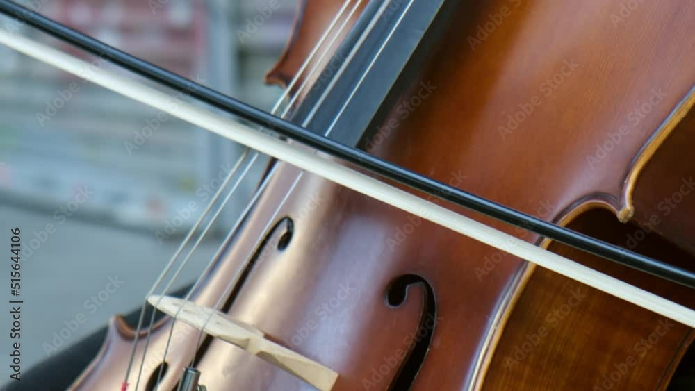 A young man is playing his cello at street in a close-up slow-motion view. There is blurry graffiti in the background. A young man is playing his cello at street in a close-up slow-motion view. There is blurry graffiti in the background.