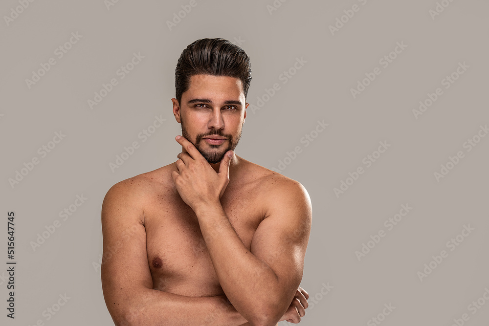 Handsome sexy man with brown eyes posing shirtless on grey studio background. Muscular body. Skin care. Handsome sexy man with brown eyes posing shirtless on grey studio background. Muscular body. Skin care.